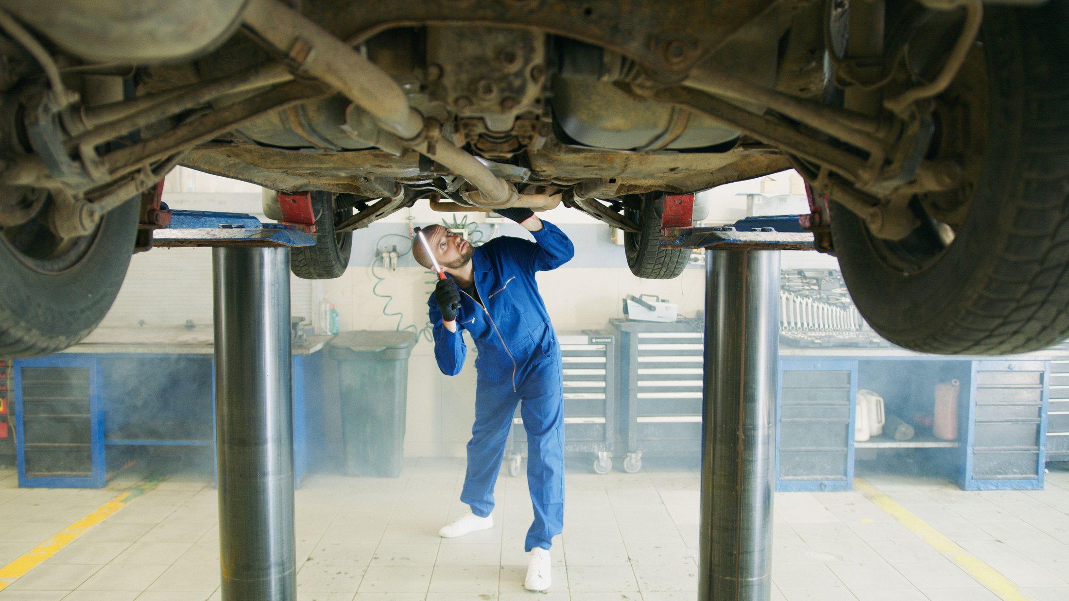 Mechaniker prüft die Unterseite eines angehobenen Fahrzeugs in einer Werkstatt